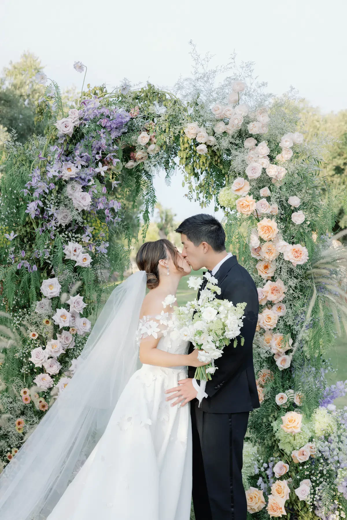 Bride And Groom Kissing Under Wedding Floral Arch